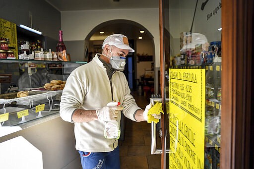 A man disinfects a shop door entrance in the town of Codogno, in the region of Lombardia, northern Italy, Wednesday, March 11, 2020. The Lombardy cluster of COVID-19 was first registered in the tiny town of Codogno on Feb. 19, when the first patient tested positive and has been a red zone until the end of seclusion and return of production in the recent days. For most people, the new coronavirus causes only mild or moderate symptoms, such as fever and cough. For some, especially older adults and people with existing health problems, it can cause more severe illness, including pneumonia. (Claudio Furlan/LaPresse via AP)