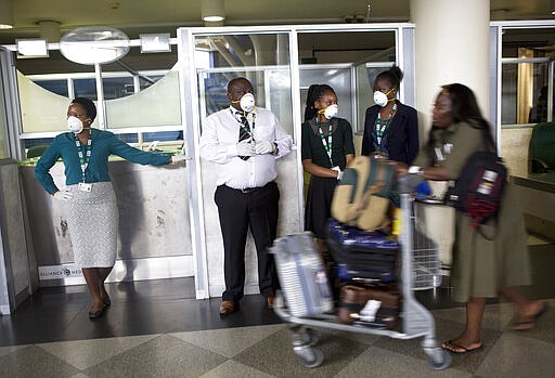 Travellers and airport staff, some wearing masks as a precaution against the coronavirus outbreak, walk through Robert Mugabe International airport in Harare, Wednesday, March, 11, 2020. For most people, the new coronavirus causes only mild or moderate symptoms, such as fever and cough. For some, especially older adults and people with existing health problems, it can cause more severe illness, including pneumonia. (AP Photo/Tsvangirayi Mukwazhi)