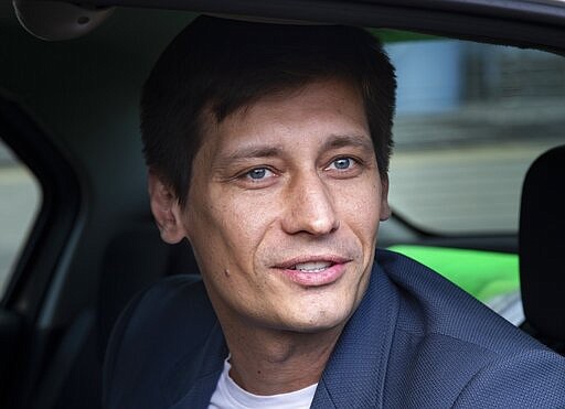 FILE - In this file photo taken on Tuesday, July 30, 2019, Russian opposition candidate Dmitry Gudkov speaks to journalists sitting inside a police car as he arrives to the court in Moscow, Russia. Gudkov, a former lawmaker turned opposition politician, believes an early parliamentary election is likely, the Kremlin would want the vote to be this year instead of next. (AP Photo/Alexander Zemlianichenko, File)