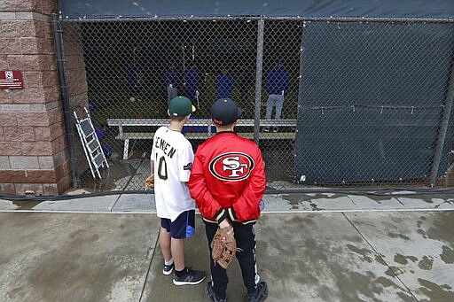 Jackson Starbuck, left, and Raymond Nylen, both 12 and from Fresno, Calif., watch Texas Rangers at batting practice after the cancellation of a spring training baseball game on the adjacent field between the Kansas City Royals and the Seattle Mariners, Thursday, March 12, 2020, in Surprise, Ariz. Major League Baseball is delaying the start of its season by at least two weeks because of the coronavirus outbreak and has suspended the rest of its spring training game schedule. (AP Photo/Elaine Thompson)