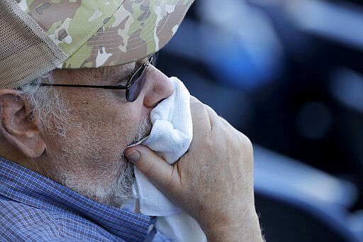 A spectator uses a towel to cover his mouth as he watches the ninth inning of a spring training baseball game between the New York Yankees and the Washington Nationals, Thursday, March 12, 2020, in West Palm Beach, Fla. Major League Baseball is delaying the start of its season by at least two weeks because of the coronavirus outbreak and has suspended the rest of its spring training game schedule. (AP Photo/Julio Cortez)