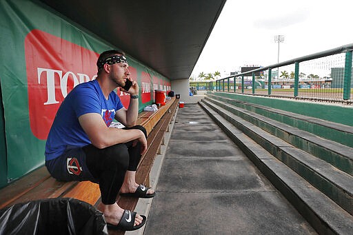 Minnesota Twins catcher Mitch Garver talks on his phone in an empty dugout at Hammond Stadium, Thursday, March 12, 2020, in Fort Myers, Fla. Major League Baseball has suspended the rest of its spring training game schedule because if the coronavirus outbreak. The league is also delaying the start of its regular season by at least two weeks. (AP Photo/Elise Amendola)