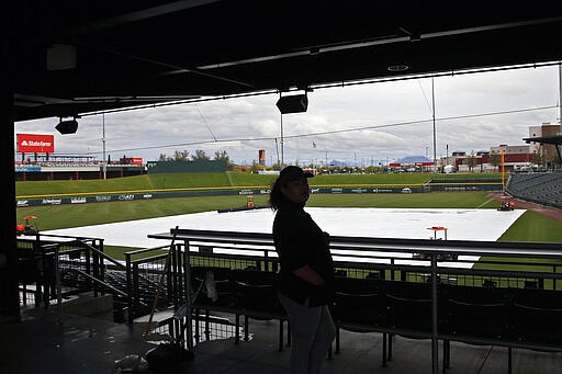 A worker looks out onto the tarp-covered field after a spring training baseball game between the Los Angeles Dodgers and the Chicago Cubs was cancelled for inclement weather, at Sloan Park in Mesa, Ariz., Thursday, March 12, 2020. Major League Baseball is delaying the start of its season by at least two weeks because of the coronavirus outbreak. Opening day had been scheduled for March 26. MLB also has suspended the rest of its spring training game schedule. (AP Photo/Sue Ogrocki)