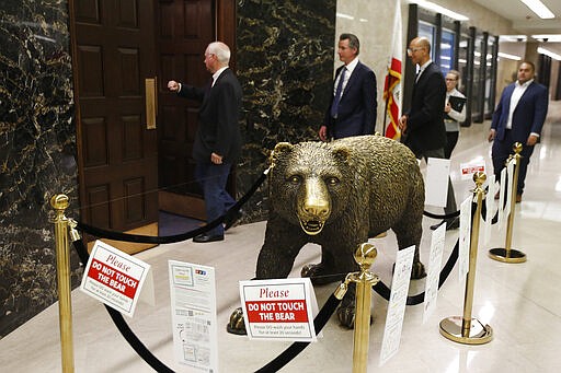 California Gov. Gavin Newsom, second from left, passes the sculpture of a bear outside his Capitol office, in Sacramento, Calif., Thursday, March 12, 2020. Mounting concerns about the coronarvirus spread to state capitols across the country on Thursday, as some lawmakers shut down their sessions, shut out the public and scrambled to finish work on essential spending bills to keep government going. (AP Photo/Rich Pedroncelli)