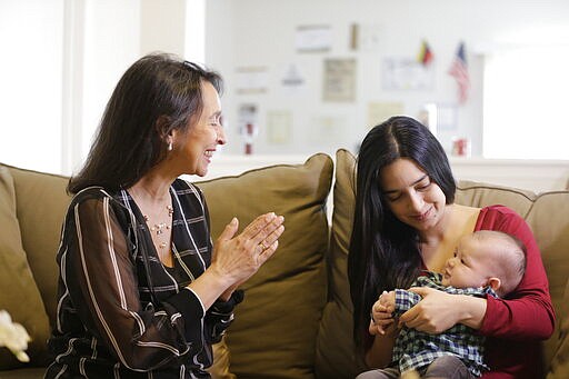 In this March 6, 2020 photo, Cioly Zambrano smiles at her three-month-old grandson held by his mother Maria Fernanda Rangel, in her home in Orlando, Florida. Zambrano, is one of 32 jurists named to the Supreme Court by opposition leader Juan Guaido, immediately converting her and her family into high-priority targets for arrest. Her son  Jose Ramon Zambrano who is the baby's father and his wife Marisa Fernanda fled Venezuela the same day Nicolas Maduro&#146;s feared intelligence police raided his family&#146;s B&amp;B. (AP Photo/Cody Jackson)