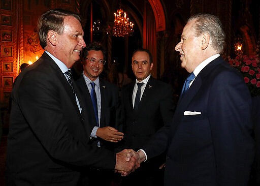 In this March 7, 2020 photo provided by Brazil's presidential press office, Brazil's President Jair Bolsonaro, left, and his Communications Director Fabio Wajngarten, second from left, greet an unidentified man during a dinner in Florida. Wajngarten tested positive for the new coronavirus, just days after the trip, according to Bolsonaro's communications office on Thursday, March 12, 2020. (Alan Santos/Brazil's presidential press office via AP)