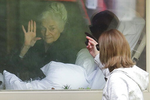 FILE - In this March 11, 2020, file photo, Judie Shape, left, who has tested positive for the coronavirus, waves to her daughter, Lori Spencer, right, as they visit on the phone and look at each other through a window at the Life Care Center in Kirkland, Wash., near Seattle. In-person visits are not allowed at the nursing home. (AP Photo/Ted S. Warren, File)