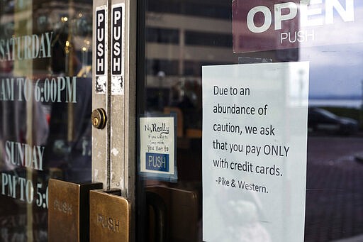 A sign posted on a door at a store near Pike Place Market, an area tourist attraction, requests credit card payments only, Wednesday, March 11, 2020, in Seattle. In efforts to slow the spread of the new coronavirus, Washington state Gov. Jay Inslee announced a ban on large public gatherings in three counties in the metro Seattle area. (AP Photo/Stephen Brashear)