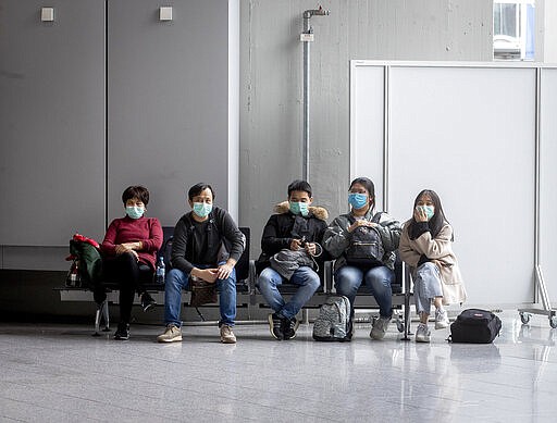 A group of passengers with face masks as protection against the coronavirus  wait for their flights in a terminal at the airport in Frankfurt, Germany, Thursday, March 12, 2020. For most people, the new coronavirus causes only mild or moderate symptoms, such as fever and cough. For some, especially older adults and people with existing health problems, it can cause more severe illness, including pneumonia. (AP Photo/Michael Probst)