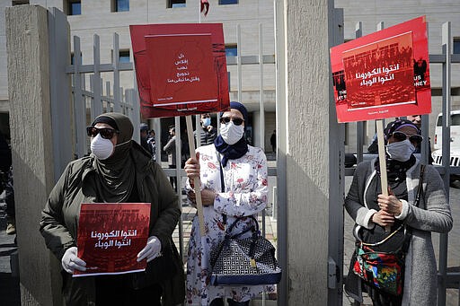 FILE - In this Feb. 26, 2020 file photo, anti-government protesters hold up banners in Arabic that read, &quot;You are the coronavirus, you are the epidemic,&quot; and &quot;Humiliation, bankruptcy, looting, starving and killing the rest of us,&quot; in front of the Lebanese Ministry of Health, in Beirut, Lebanon. As 2019 gave way to 2020 in a cloud of tear gas, and in some cases a hail of bullets - it seemed civil disobedience and government responses to protests would dominate the international landscape. Then came the Coronavirus. The protest camps in central Beirut are subdued. Masks worn to protect against tear gas are more often now worn to protect against the virus. The vast majority of people recover from the new virus. (AP Photo/Hassan Ammar, File)