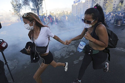 FILE - In this December 20, 2019, file photo, anti-government demonstrators run from a cloud of teargas during clashes with police in Santiago, Chile. Last year, face masks were an act of rebellion, a signature piece of clothing associated with protesters in  who wore them to protect against tear gas or to conceal their identities from authorities. These same masks are now ubiquitous around the world -- worn by people from China and Iran, to Italy and America, seeking to protect against the coronavirus. The vast majority of people recover from the new virus. (AP Photo/Fernando Llano)