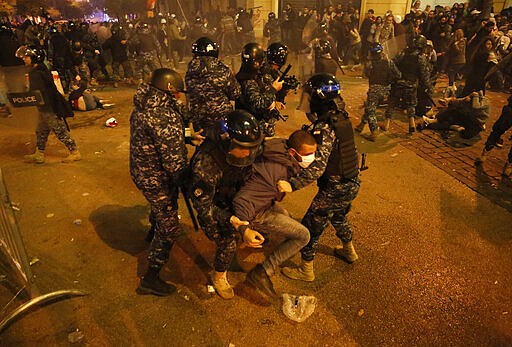 FILE - In this Dec. 15, 2019 file photo, riot police officers beat anti-government protesters near the parliament square, in downtown Beirut, Lebanon. Last year, face masks were an act of rebellion, a signature piece of clothing associated with protesters who wore them to protect against tear gas or to conceal their identities from authorities. These same masks are now ubiquitous around the world -- worn by people from China and Iran, to Italy and America, seeking to protect against the coronavirus. The vast majority of people recover from the new virus. (AP Photo/Hussein Malla, File)