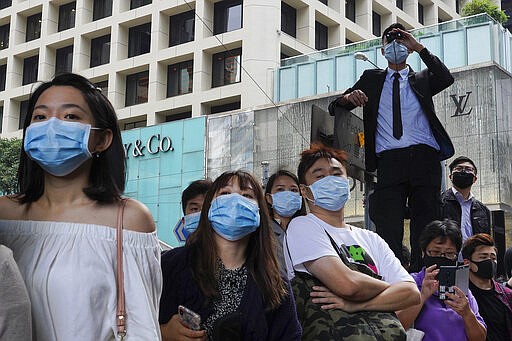 FILE - In this Nov. 12, 2019 file photo, people wearing face masks watch pro-democracy protesters in Central, Hong Kong. In 2019, face masks were the signature of Hong Kong&#146;s protesters, who wore them to protect against tear gas and conceal their identities from authorities. These same masks are now ubiquitous around the world -- a hallmark of the spreading coronavirus worn by people from China and Iran, to Italy and America, seeking to protect against the  new coronavirus. The vast majority of people recover from the new virus. (AP Photo/Vincent Yu, File)