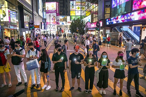 FILE - In this Oct. 18, 2019, file photo, protestors wearing masks stand along a commercial shopping street in Hong Kong. Last year, face masks were the signature of Hong Kong&#146;s protesters, who wore them to protect against tear gas and conceal their identities from authorities. These same masks are now ubiquitous around the world -- worn by people from China and Iran, to Italy and America, seeking to protect against the coronavirus. The vast majority of people recover from the new virus. (AP Photo/Mark Schiefelbein, File)