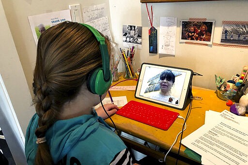 In this photo provided by Anne Marie Canlis,  Clementine Canlis, of Seattle, watches an online lecture Thursday, March 12, 2020, after her private school closed for five weeks due to the coronavirus. The Canlis family's three children, ages 14, 11 and 9, are split between two private schools that are closed for six weeks and five weeks, respectively. Canlis' husband's family owns a well-known, award-winning restaurant called Canlis that will close next week and instead open three different options: a bagel shop, a drive-thru burger stand in the restaurant parking lot and a home delivery meal service for cooped up families. For most people, the new coronavirus causes only mild or moderate symptoms. For some it can cause more severe illness. (Anne Marie Canlis via AP)