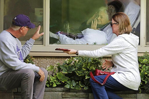 Judie Shape, center, who has tested positive for the coronavirus, blows a kiss to her son-in-law, Michael Spencer, left, as Shape's daughter, Lori Spencer, right, looks on, Wednesday, March 11, 2020, as they visit on the phone and look at each other through a window at the Life Care Center in Kirkland, Wash., near Seattle. In-person visits are not allowed at the nursing home.  The vast majority of people recover from the new coronavirus. According to the World  Health Organization, most people recover in about two to six weeks, depending on the severity of the illness. (AP Photo/Ted S. Warren)