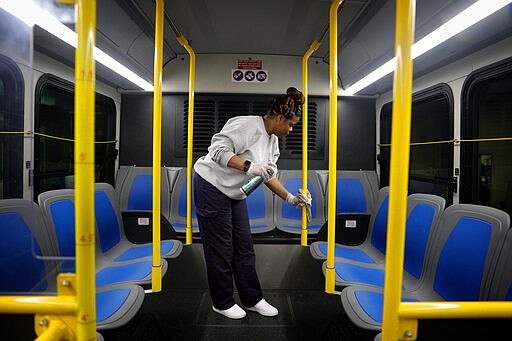 Stacy Loggins, a janitorial supervisor for Metro, wipes down the interior of a bus with disinfectant Thursday, March, 12, 2020, at a Metro facility in St. Louis. Metro cleaners have been asked to be sure to change towels frequently and wear two pairs of gloves as they perform cleaning tasks. (Christian Gooden/St. Louis Post-Dispatch via AP)