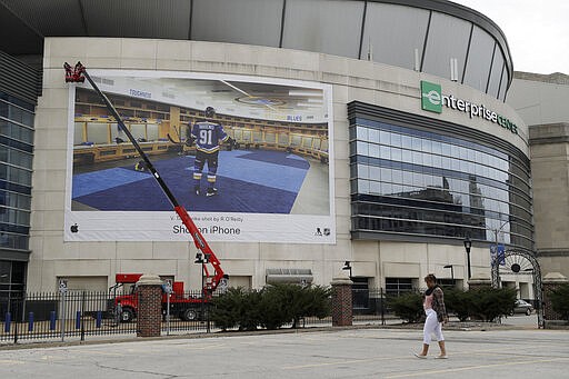 Workers use a lift to maintain a large banner of St. Louis Blues' Vladimir Tarasenko hanging on the side of Enterprise Center, home of the St. Louis Blues hockey team, Friday, March 13, 2020, in St. Louis. The Blues' season, along with the rest of the NHL, has been suspended in an effort to contain the COVID-19 virus. (AP Photo/Jeff Roberson)