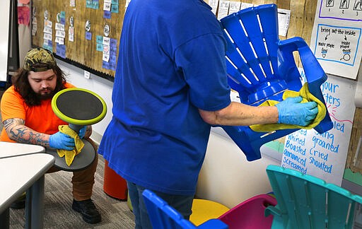 Custodians Steven Bassett, left, and Cathy Rego clean chairs inside a first grade classroom at Eureka Elementary school as the Rockwood School District begins a weeklong break on Friday, March 13, 2020. Custodians started deep cleaning the first of 33 buildings using mist sprayers and disinfectant to fight the spread of the coronavirus. (Robert Cohen/St. Louis Post-Dispatch via AP)