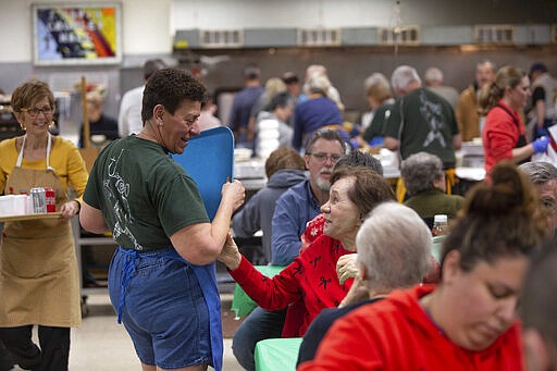 In this Feb. 28, 2020 photo, Ann Painter, center, is greeted by a diner as she serves meals during the a fish fry at Holy Angels parish in Pittsburgh, Pa. On March 12, Pittsburgh Bishop David Zubik suggested that people enjoy the fish fries with a take-out order rather than dining in due to virus concerns. (AP Photo/Rebecca Droke)