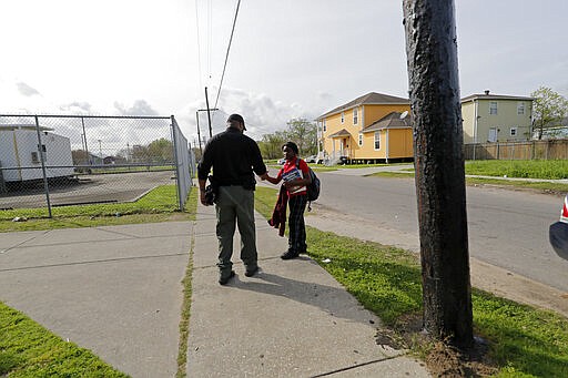 School Resource Officer Donald Lee hands a cell phone back to a student who was calling for her ride after school was adjourned at the Dr.Martin Luther King, Jr. Elementary School for Science and Technology in New Orleans, Friday, March 13, 2020. Louisiana Gov. John Bel Edwards on Friday closed K-12 public schools across the state for roughly a month and banned gatherings of more than 250 people in an effort to slow the spread of the coronavirus.For most people, the new coronavirus causes only mild or moderate symptoms. For some it can cause more severe illness. (AP Photo/Gerald Herbert)