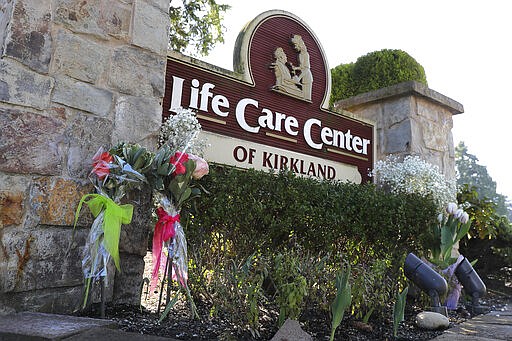 Flowers left next to the sign that marks the entrance to the parking lot of the Life Care Center in Kirkland, Wash. are shown Monday, March 9, 2020, near Seattle. The nursing home is at the center of the outbreak of the COVID-19 coronavirus in Washington state. (AP Photo/Ted S. Warren)