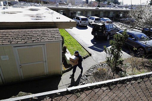 A U.S. Public Health Services worker carries boxes of supplies to a back entrance of the Life Care Center in Kirkland, Wash., Monday, March 9, 2020, near Seattle. The nursing home is at the center of the outbreak of the new coronavirus in Washington state. (AP Photo/Ted S. Warren)