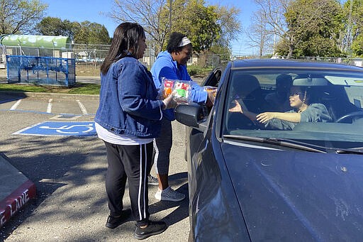 In this Tuesday, March 10, 2020, photo, Florin Elementary School staff hand out food to students and parents driving in, after their facility closed in response to the coronavirus Sacramento, Calif. (AP Photo/Cuneyt Dil)