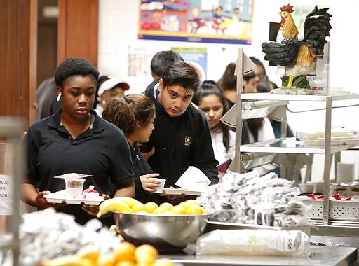 Students line up for lunch in the cafeteria at Lincoln High School in Dallas, Friday, March 13, 2020. During the coming extended spring break school closures, this cafeteria and others in the Dallas Independent School District will be providing lunches to students despite the closure of the school. (AP Photo/LM Otero)