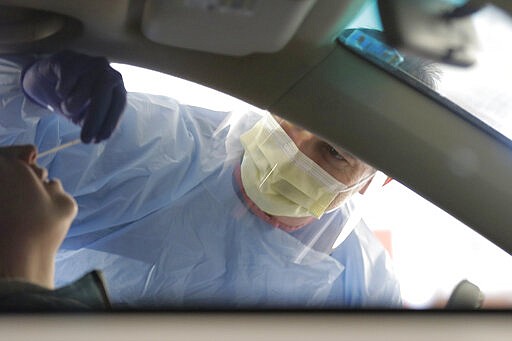 A nurse at a drive-up coronavirus testing station set up by the University of Washington Medical Center uses a swab to take a sample from the nose of a person in a car Friday, March 13, 2020, in Seattle. UW Medicine is conducting  testing in a hospital parking garage and has screened hundreds of staff members, faculty and trainees for COVID-19. U.S. hospitals are setting up triage tents, calling doctors out of retirement, guarding their supplies of face masks and making plans to cancel elective surgery as they brace for an expected onslaught of coronavirus patients. (AP Photo/Ted S. Warren)