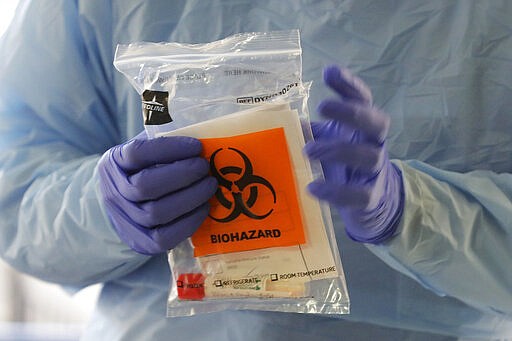 A nurse at a drive up COVID-19 coronavirus testing station, set up by the University of Washington Medical Center, holds a bag containing a swab used to take a sample from the nose of a person in their car, Friday, March 13, 2020, in Seattle. UW Medicine is conducting drive-thru testing in a hospital parking garage and has screened hundreds of staff members, faculty and trainees for the COVID-19 coronavirus. U.S. hospitals are setting up triage tents, calling doctors out of retirement, guarding their supplies of face masks and making plans to cancel elective surgery as they brace for an expected onslaught of coronavirus patients. (AP Photo/Ted S. Warren)