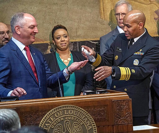 U.S. Surgeon General VADM Jerome M. Adams, M.D., M.P.H., right, squirts hand sanitizer into Gov. John Bel Edwards, left, palm as the pair talk about the coronavirus at a press conference at the state capital Thursday March 12, 2020, in Baton Rouge, La. (Bill Feig/The Advocate via AP)/The Advocate via AP)