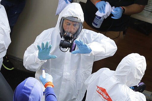 Servpro cleaning workers are sprayed as they exit the Life Care Center in Kirkland, Wash., Thursday, March 12, 2020, at the end of a day spent cleaning inside the facility near Seattle. The nursing home is at the center of the outbreak of the new coronavirus in Washington state. (AP Photo/Ted S. Warren)