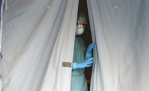 A medical staffer watches from a tent at one of the emergency structures that were set up to ease procedures at the Brescia hospital, northern Italy, Thursday, March 12, 2020. Italians woke up to yet further virus-containment restrictions after Premier Giuseppe Conte ordered restaurants, cafes and retail shops closed after imposing a nationwide lockdown on personal movement. For most people, the new coronavirus causes only mild or moderate symptoms, such as fever and cough. For some, especially older adults and people with existing health problems, it can cause more severe illness, including pneumonia. (AP Photo/Luca Bruno)