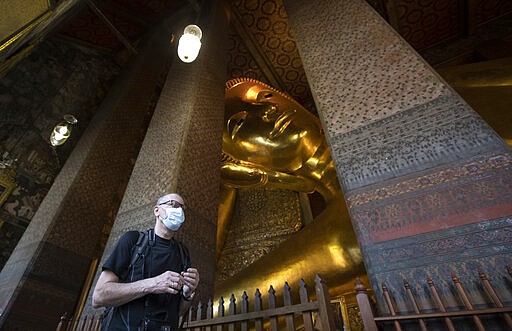 A tourist wearing protective mask walk in front of giant Buddha at Wat Pho temple in Bangkok, Thailand, Friday, March 13, 2020. For most people, the new coronavirus causes only mild or moderate symptoms. For some it can cause more severe illness. (AP Photo/Sakchai Lalit)