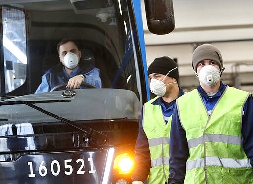 A bus depot employees walk past a disinfected bus in Moscow, Russia, Friday, March 13, 2020.For most people, the new coronavirus causes only mild or moderate symptoms, such as fever and cough. For some, especially older adults and people with existing health problems, it can cause more severe illness, including pneumonia. (Kirill Zykov, Moscow News Agency photo via AP)