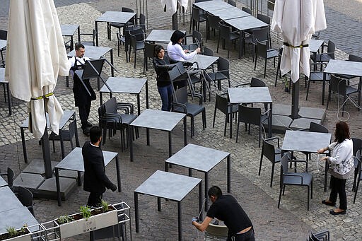 Waiters carry chairs after the town hall decreed the closure of the terraces at Mayor square in central Madrid, Spain, Friday, March 13, 2020. Exhibitions, conferences, sports centers and museums are closing in Madrid, including the Spanish capital's Prado Museum for the first time in eight decades. For some, especially older adults and people with existing health problems, it can cause more severe illness, including pneumonia. (AP Photo/Manu Fernandez)