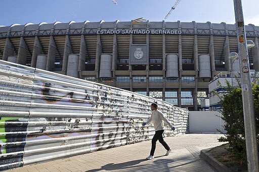 A woman wearing a protective mask walks past Real Madrid's Santiago Bernabeu stadium in Madrid, Spain, Friday, March 13, 2020. Real Madrid have said its players were being placed in isolation after one of the club's basketball players, who share facilities with Madrid's soccer players, tested positive for the COVID-19 coronavirus. That led to the instant decision by the Spanish league to bring matches to a halt for the next two rounds. For most people, the new coronavirus causes only mild or moderate symptoms. For some it can cause more severe illness, especially in older adults and people with existing health problems. (AP Photo/Paul White)