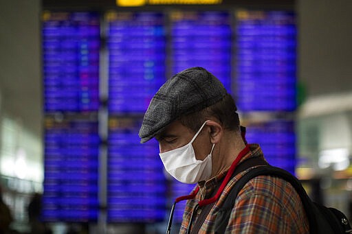 A man looks at his phone in front of the information screen at Barcelona airport, Spain, Thursday, March 12, 2020. President Donald Trump, who had downplayed the coronavirus for weeks, suddenly struck a different tone, announcing strict rules on restricting travel from much of Europe to begin this weekend. For most people, the new coronavirus causes only mild or moderate symptoms, such as fever and cough. For some, especially older adults and people with existing health problems, it can cause more severe illness, including pneumonia. (AP Photo/Emilio Morenatti)