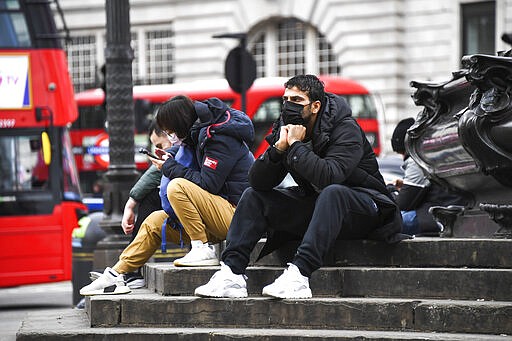 People wear face masks as they sit on the Shaftesbury Memorial Fountain in Piccadilly Circus, in London, Friday, March 13, 2020. For most people, the new coronavirus causes only mild or moderate symptoms, such as fever and cough. For some, especially older adults and people with existing health problems, it can cause more severe illness, including pneumonia.(AP Photo/Alberto Pezzali)