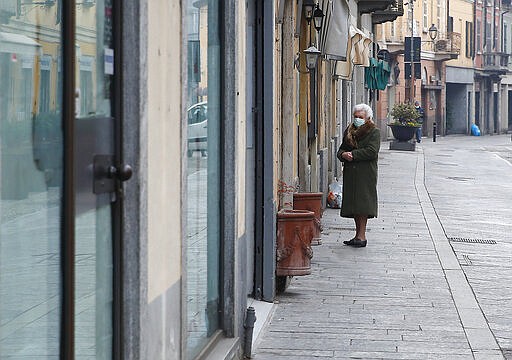 In this photo taken on Thursday, March 12, 2020, an elderly woman wearing a mask waits to enter a deli meat and cold cuts shop in Codogno, Italy. The northern Italian town that recorded Italy&#146;s first coronavirus infection has offered a virtuous example to fellow Italians, now facing an unprecedented nationwide lockdown, that by staying home, trends can reverse. Infections of the new virus have not stopped in Codogno, which still has registered the most of any of the 10 Lombardy towns Italy&#146;s original red zone, but they have slowed. For most people, the new coronavirus causes only mild or moderate symptoms. For some it can cause more severe illness. (AP Photo/Antonio Calanni)