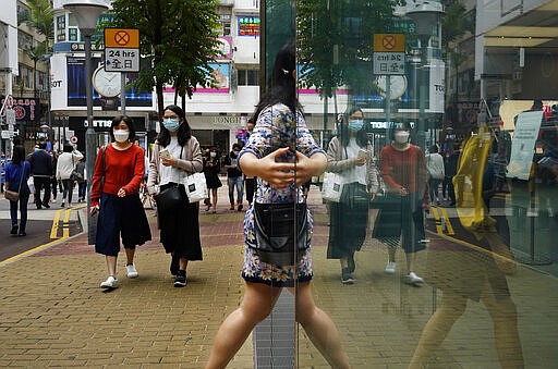 People wearing face masks walk at a street in Hong Kong Friday, March. 13, 2020. For most, the coronavirus causes only mild or moderate symptoms, such as fever and cough. But for a few, especially older adults and people with existing health problems, it can cause more severe illnesses, including pneumonia. (AP Photo/Vincent Yu)