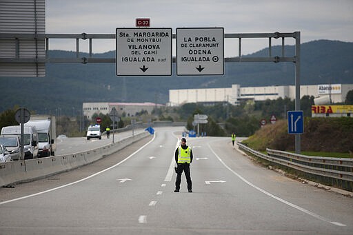 A mosso de esquadra police officer stands on the closed off road near Igualada, Spain, Friday, March 13, 2020. Over 60,000 people awoke Friday in four towns near Barcelona confined to their homes and with police blocking roads. The order by regional authorities in Catalonia is Spain's first mandatory lockdown as COVID-19 coronavirus infections increase sharply, putting a strain on health services and pressure on the government for more action.  (AP Photo/Joan Mateu)