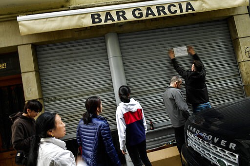 People look on as a man puts a notice informing costumers the bar is closing to prevent coronavirus, in Pamplona, northern Spain, Thursday, March 12, 2020. For most people, the new COVID-19 coronavirus causes only mild or moderate symptoms, such as fever and cough, but for some, especially older adults and people with existing health problems, it can cause more severe illness, including pneumonia.  (AP Photo/Alvaro Barrientos)