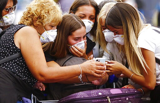 Travelers wearing protective masks look at a smart phone at the Ministro Pistarini International Airport, in Ezeiza on the outskirts of Buenos Aires, Argentina, Friday, March 13, 2020. Starting next Tuesday, Argentina is banning flights from the U.S., Europe and China, as a precaution against the spread of the new coronavirus. The vast majority of people recover from the new virus. (AP Photo/Marcos Brindicci)