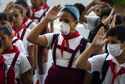 Students, some wearing protective masks as a precaution against the spread of the coronavirus, hold up their right hands as they recite the national anthem, in Havana, Cuba, Friday, March 13, 2020. For most people, the new coronavirus causes only mild or moderate symptoms, such as fever and cough. For some, especially older adults and people with existing health problems, it can cause more severe illness, including pneumonia. (AP Photo/Ramon Espinosa)