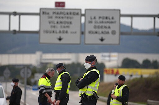 Mossos de esquadra police officers stand on the closed off road near Igualada, Spain, Friday, March 13, 2020. Over 60,000 people awoke Friday in four towns near Barcelona confined to their homes and with police blocking roads. The order by regional authorities in Catalonia is Spain's first mandatory lockdown as COVID-19 coronavirus infections increase sharply, putting a strain on health services and pressure on the government for more action. For most people, the new coronavirus causes only mild or moderate symptoms, such as fever and cough. For some, especially older adults and people with existing health problems, it can cause more severe illness, including pneumonia. (AP Photo/Joan Mateu)