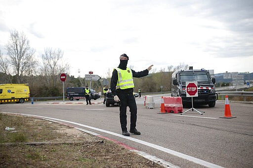 A police officer signals to approching traffic on the closed off road near Igualada, Spain, Friday, March 13, 2020. Over 60,000 people awoke Friday in four towns near Barcelona confined to their homes and with police blocking roads. The order by regional authorities in Catalonia is Spain's first mandatory lockdown as COVID-19 coronavirus infections increase sharply, putting a strain on health services and pressure on the government for more action. For most people, the new coronavirus causes only mild or moderate symptoms, such as fever and cough. For some, especially older adults and people with existing health problems, it can cause more severe illness, including pneumonia. (AP Photo/Joan Mateu)