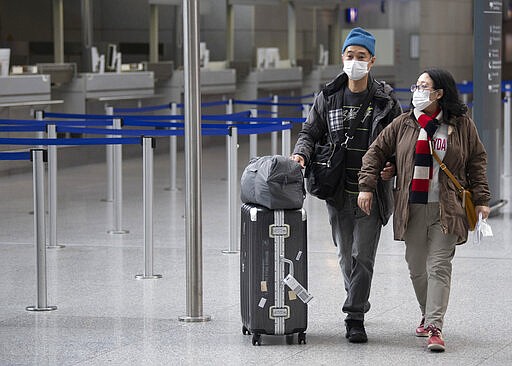 Two passengers wearing masks make their way through the terminal at Frankfurt airport, Germany, Friday March 13, 2020. Due to the Coronavirus a large number of flights have to be cancelled. For most people, the new coronavirus causes only mild or moderate symptoms, such as fever and cough. For some, especially older adults and people with existing health problems, it can cause more severe illness, including pneumonia.(Boris Roessler/DPA via AP)