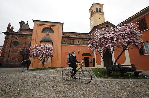 In this photo taken on Thursday, March 12, 2020, a woman wearing a mask rides a bicycle in Codogno, Italy. The northern Italian town that recorded Italy&#146;s first coronavirus infection has offered a virtuous example to fellow Italians, now facing an unprecedented nationwide lockdown, that by staying home, trends can reverse. Infections of the new virus have not stopped in Codogno, which still has registered the most of any of the 10 Lombardy towns Italy&#146;s original red zone, but they have slowed. For most people, the new coronavirus causes only mild or moderate symptoms. For some it can cause more severe illness. (AP Photo/Antonio Calanni)